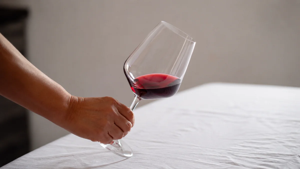 Calice di vino rosso inclinato su tovaglia bianca durante l analisi visiva della degustazione