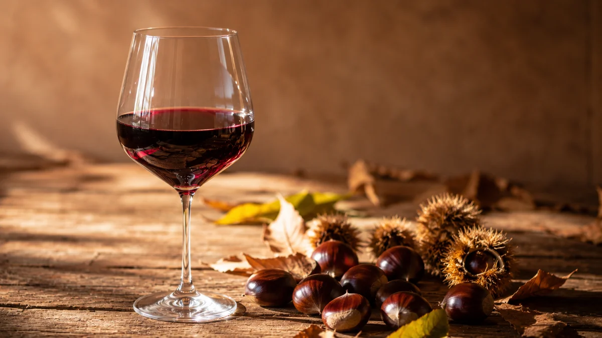 Calice di vino novello dai riflessi violacei accanto a castagne, abbinamento autunnale